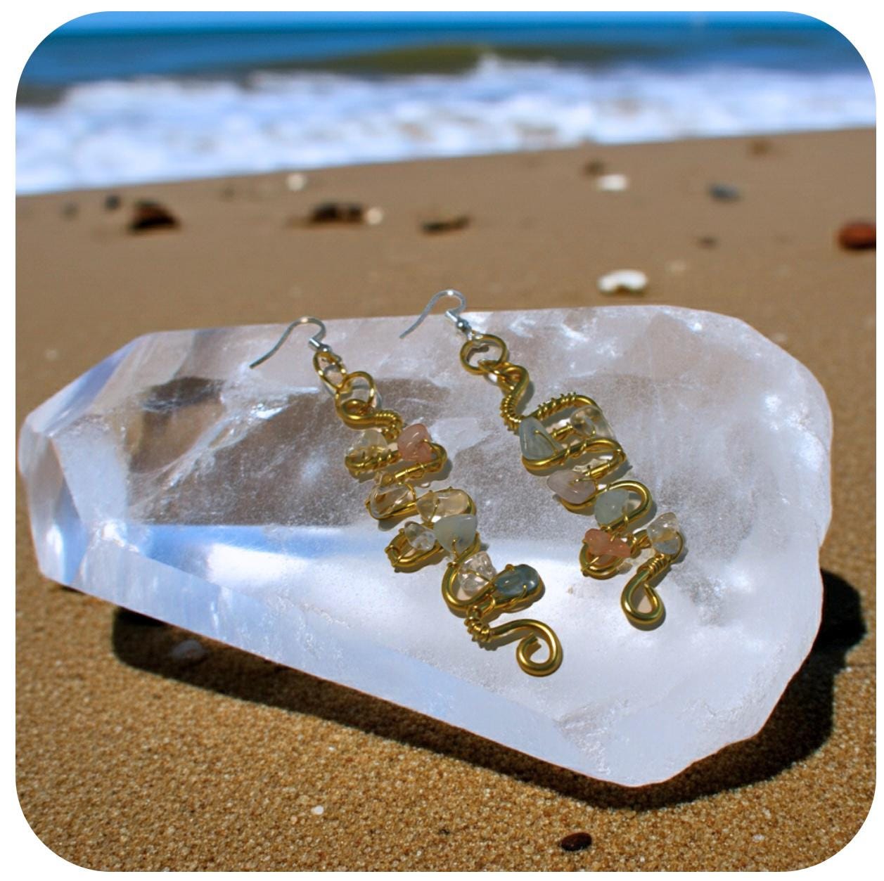 Copper and gemstone earrings on a clear crystal with a beach background