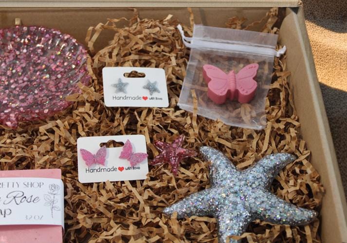 Box of rose scented handmade soap and matching mini butterfly rose scented soap, a resin starfish, pink butterfly stud earrings, and glitter starfish earrings on paper in a gift set.