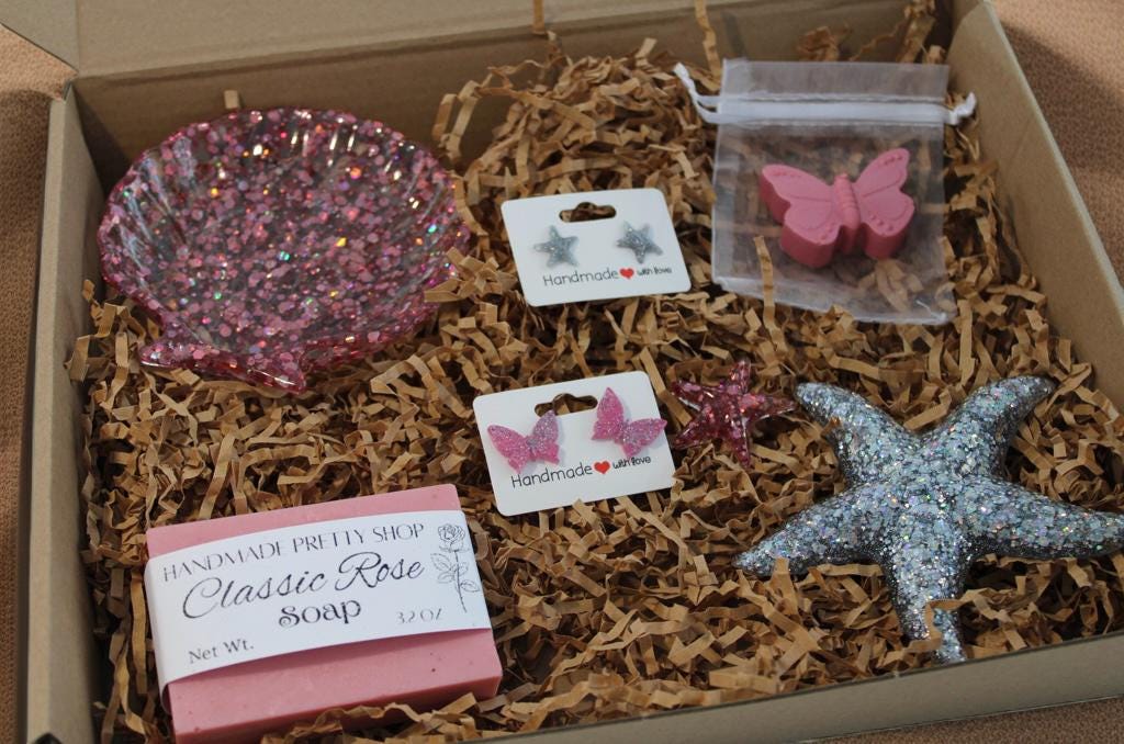 Box of rose scented handmade soap and matching mini butterfly rose scented soap, a resin starfish, pink butterfly stud earrings, and glitter starfish earrings on paper in a gift set.