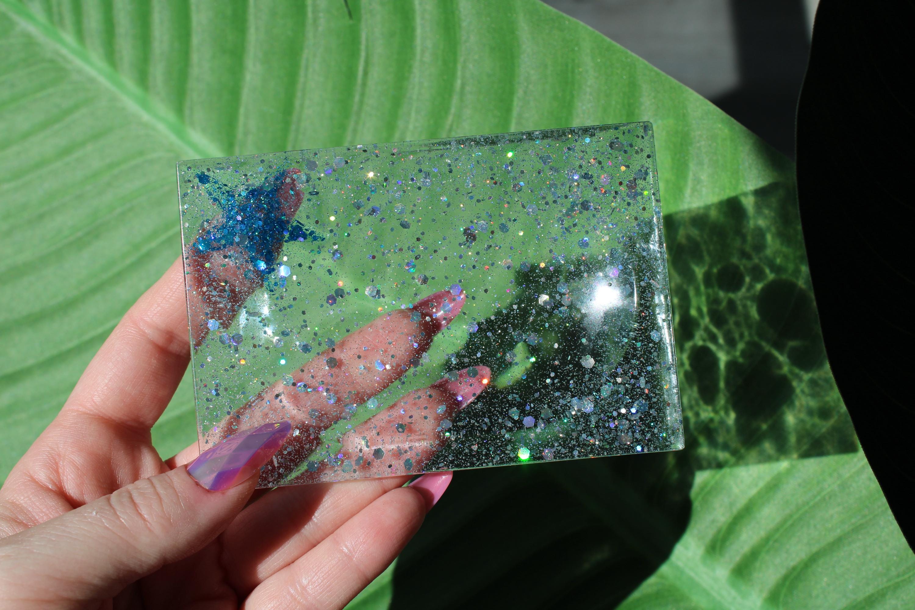 Hand holding a clear soap dish with glittery sequins and a blue starfish against a green leaf background