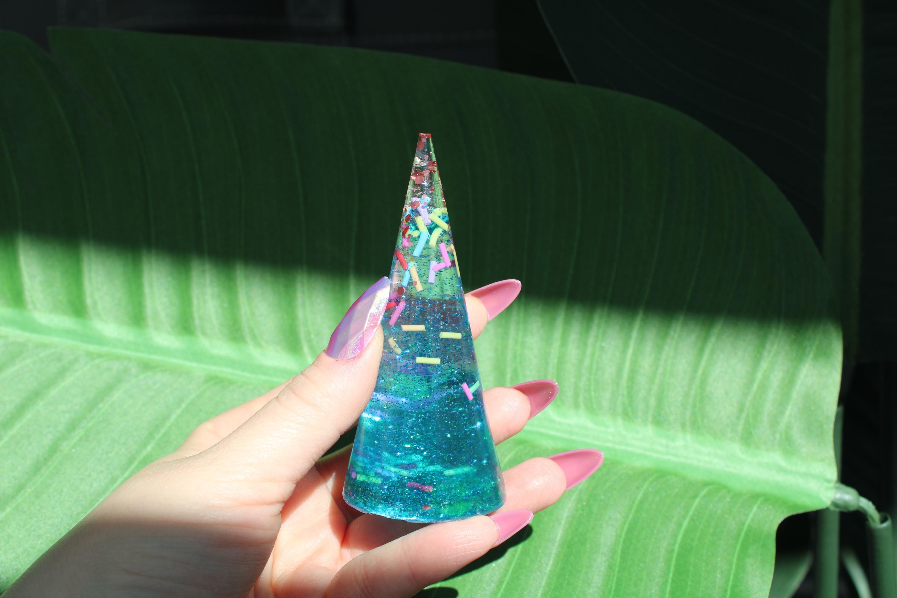 Hand holding a colorful, translucent cone-shaped ring holder against a green leaf background