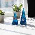 Two blue jewelry display cones with jewelry on a desk with plants and a laptop in the background.