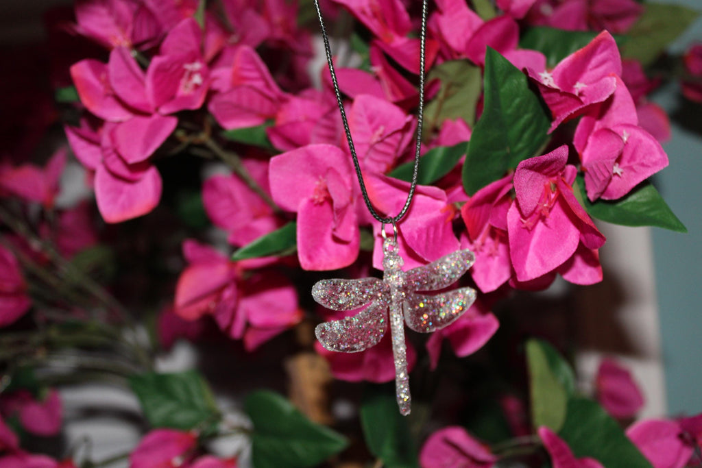 Dragonfly-shaped pendant on a chain against a pink floral background