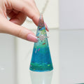 Hand holding a colorful ring holder display with sprinkles inside and with a ring on it, against a light background