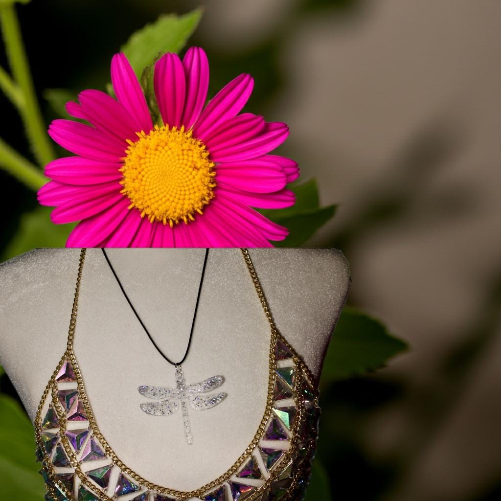 Necklace with a dragonfly pendant displayed on a mannequin bust with a pink flower in the background.