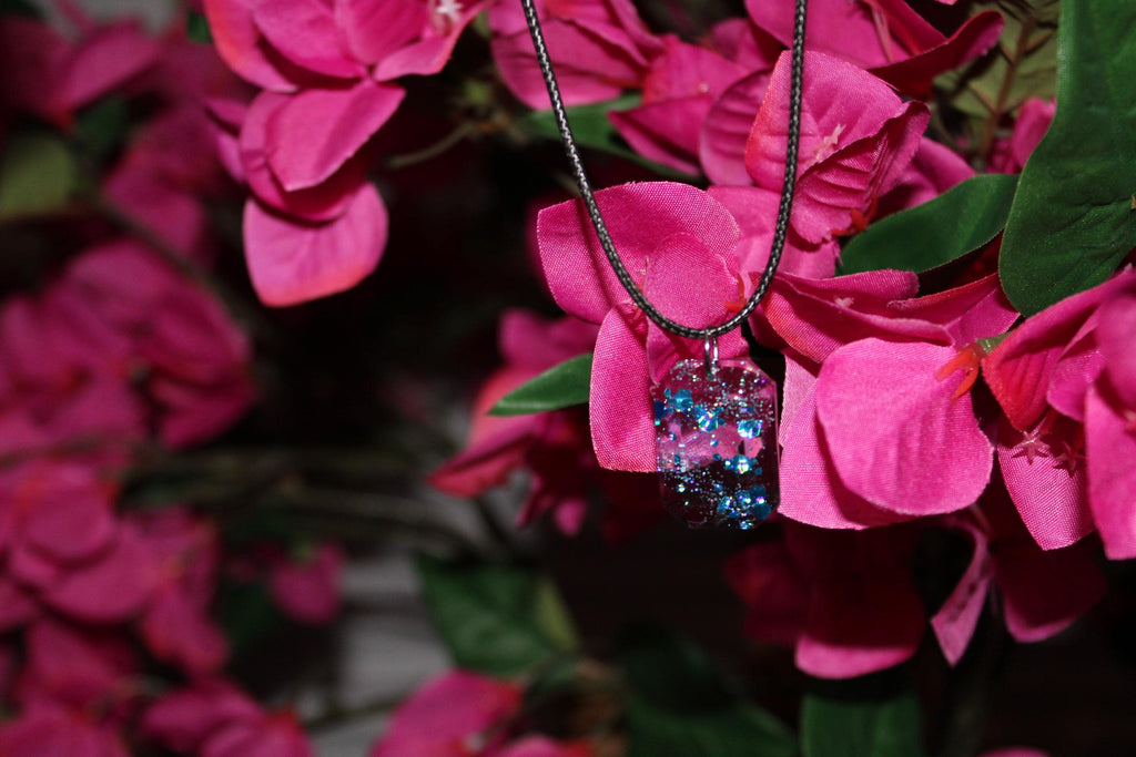 Necklace with a blue and clear pendant hanging on pink flowers