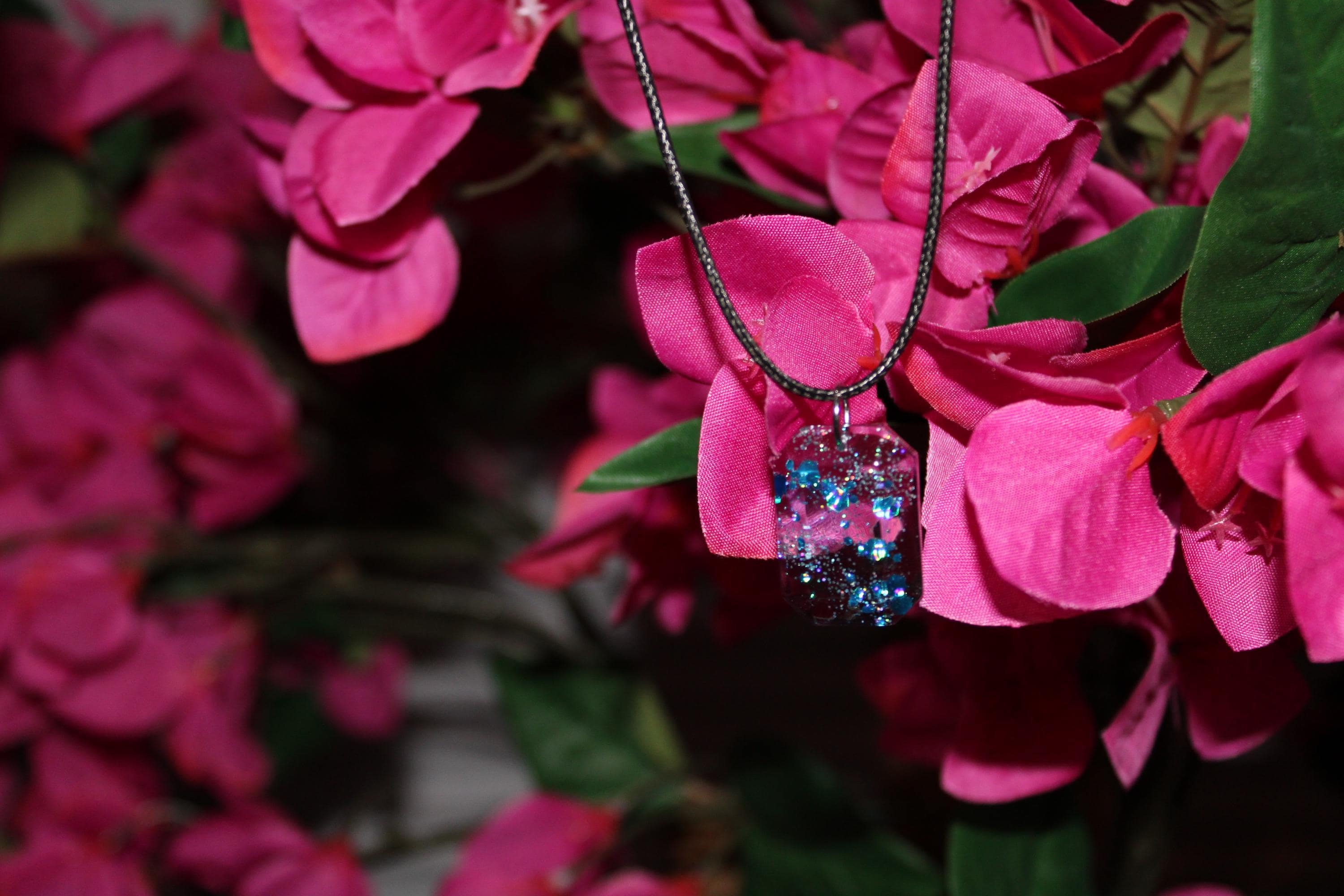 Necklace with a blue and clear pendant hanging on pink flowers