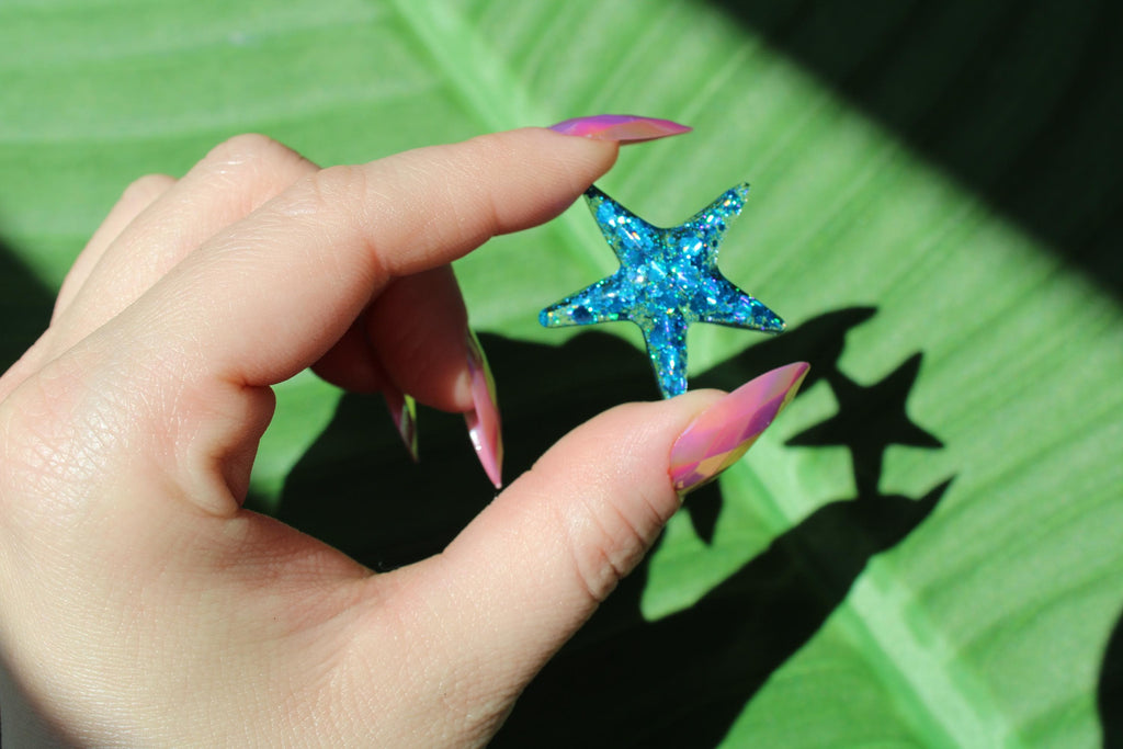 Hand holding a blue sequin starfish against a green background