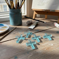 Blue resin crosses on a wooden table with art supplies in the background