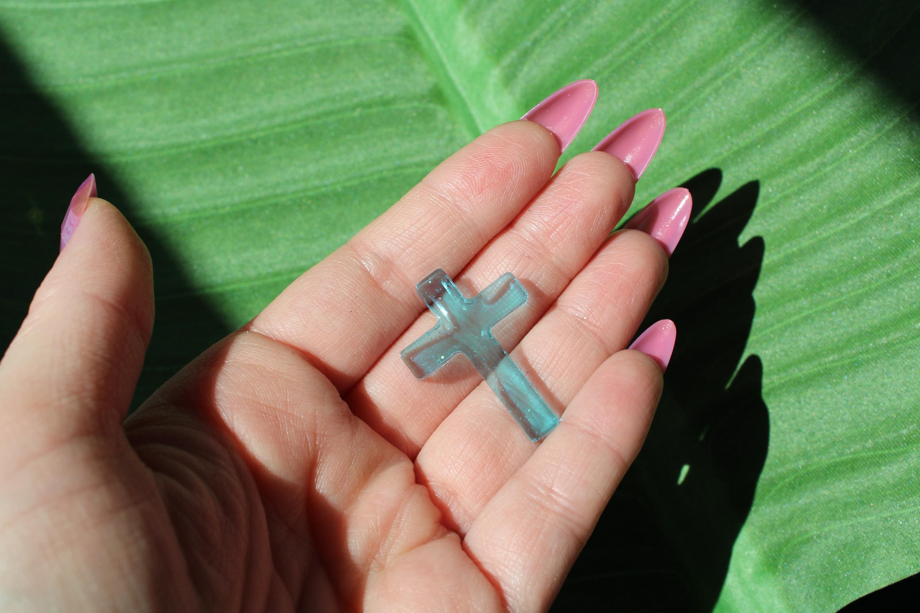 Hand holding a small resin cross against a green leaf background