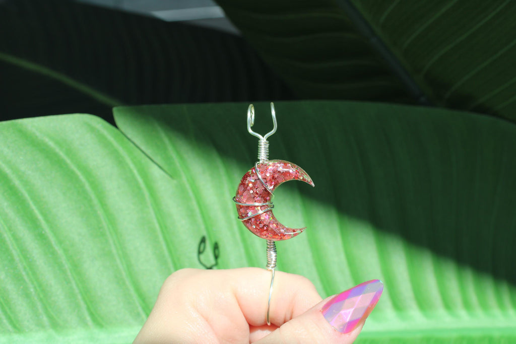 Pink crescent moon-shaped smoke ring held by a hand with green leaves in the background
