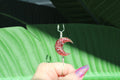 Pink crescent moon-shaped smoke ring held by a hand with green leaves in the background