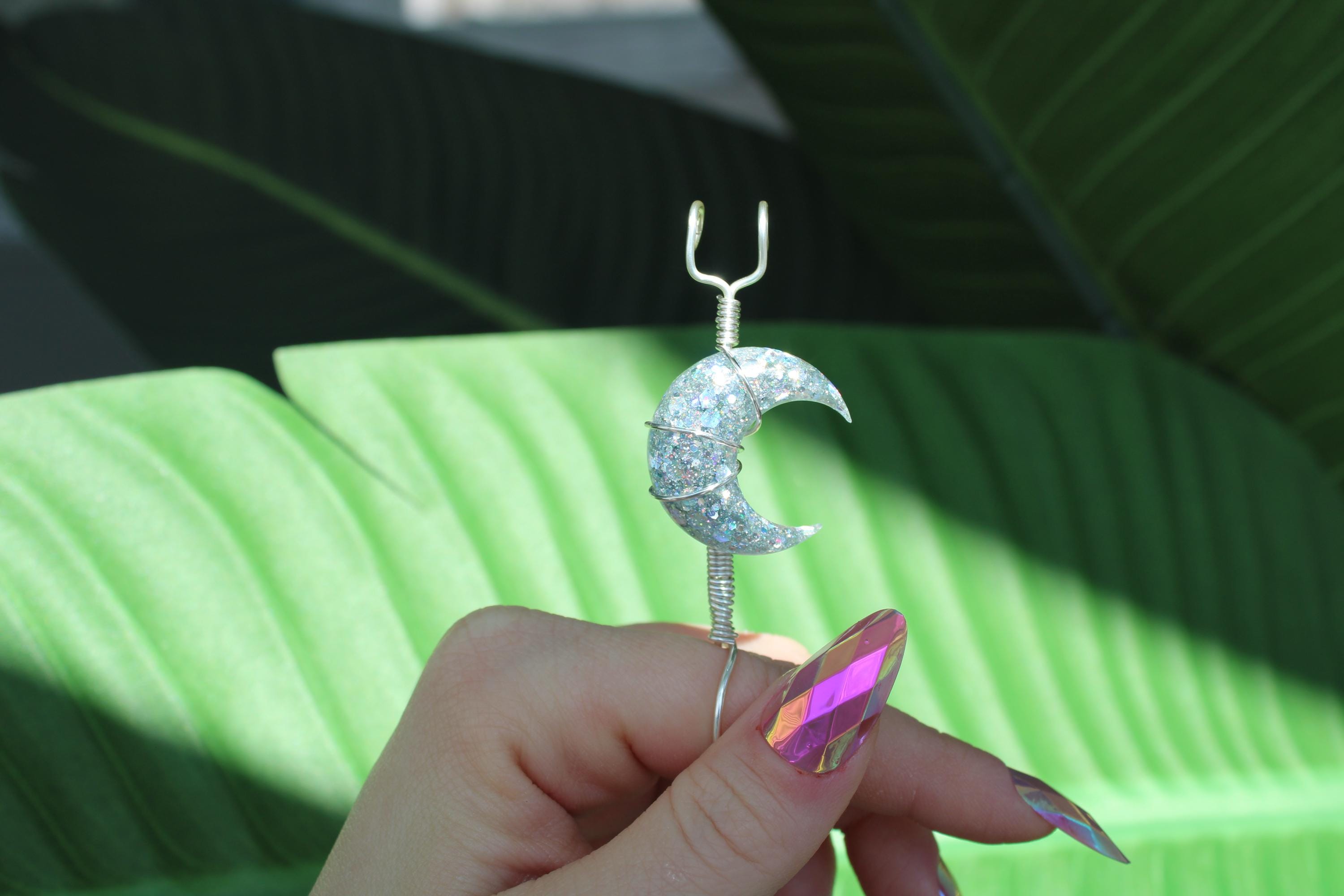 Hand holding a smoke ring with a crescent moon design against a green leafy background