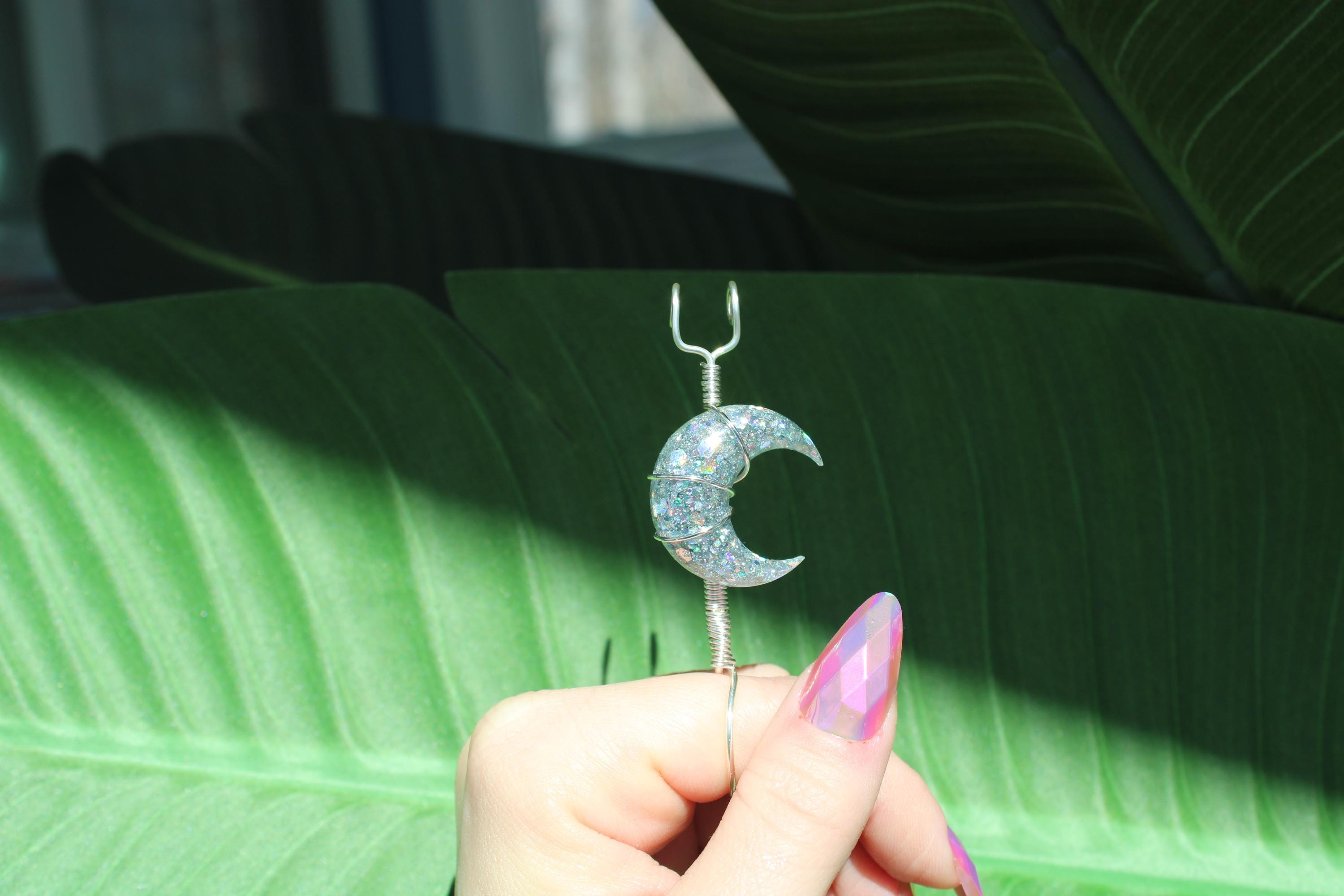 Decorative smoke ring with a crescent moon design held by a hand against a green leafy background