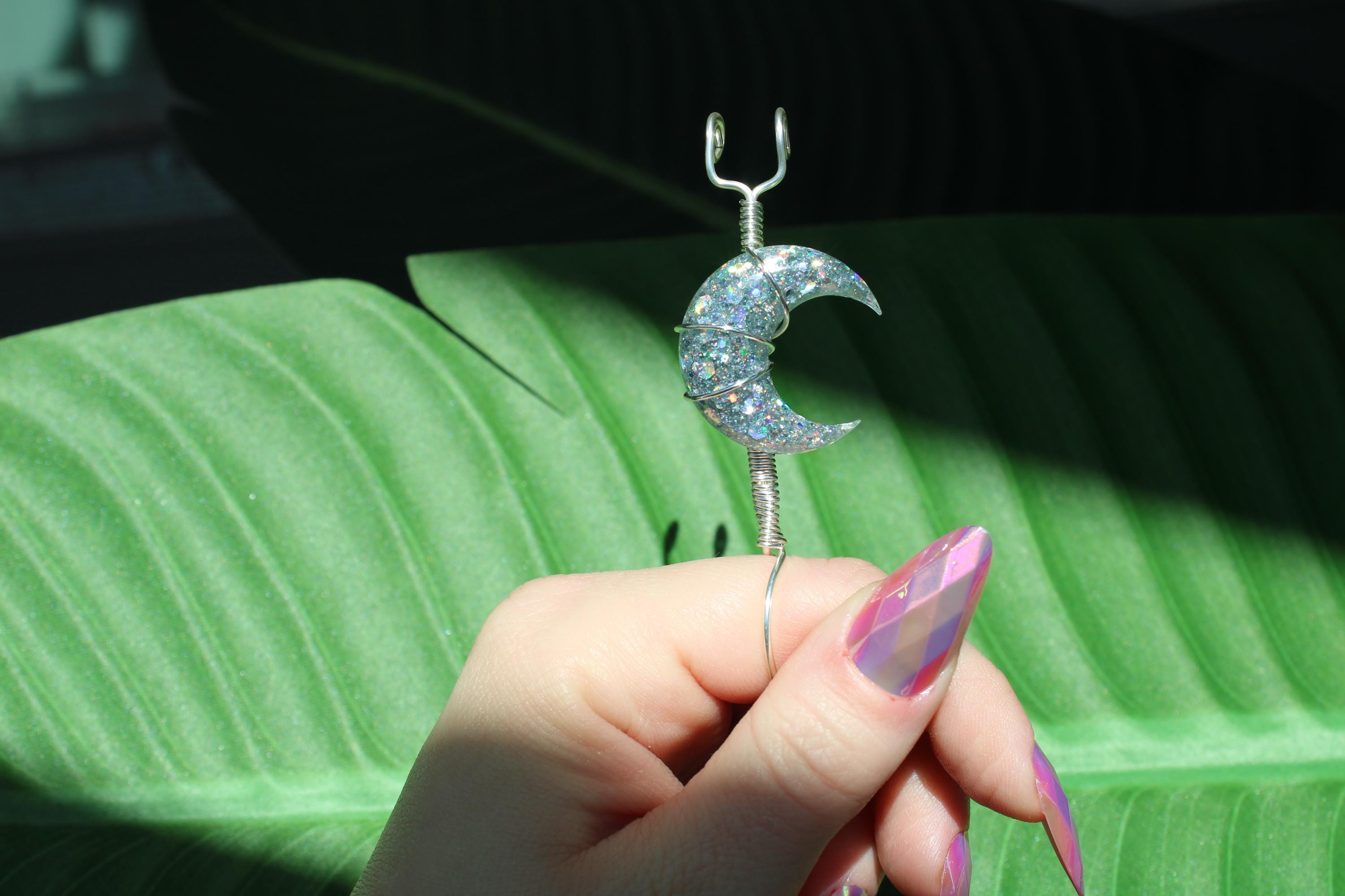 Hand holding a smoke ring with a crescent moon design against a green leaf background
