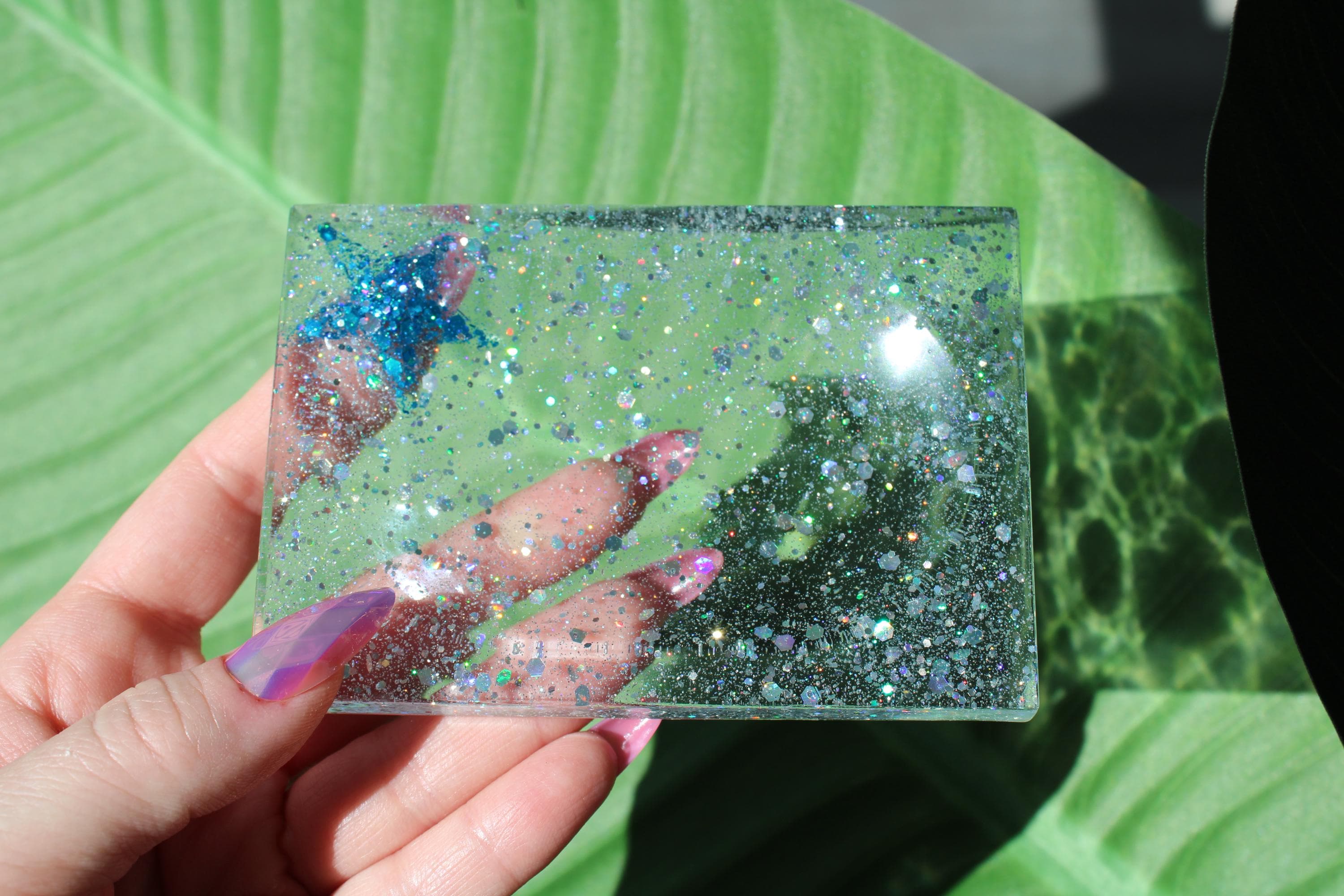 Hand holding a starfish soap dish with glitter against a green leafy background.