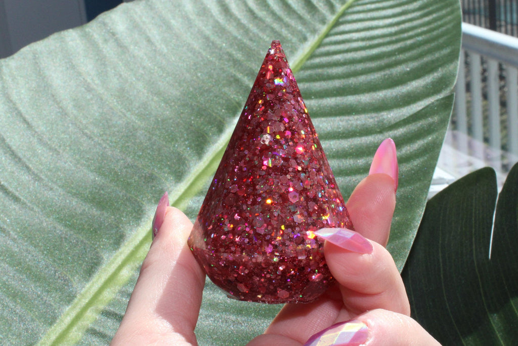 Hand holding a glittery pink ring holder cone against a leafy background