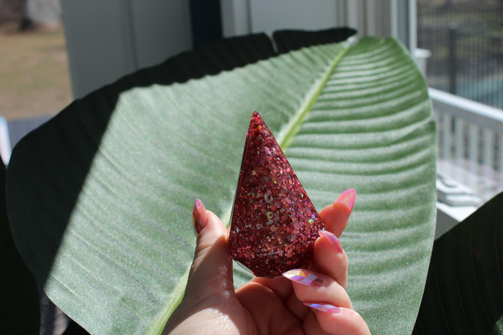 Hand holding a pink glittery ring holder cone against a large green leaf.