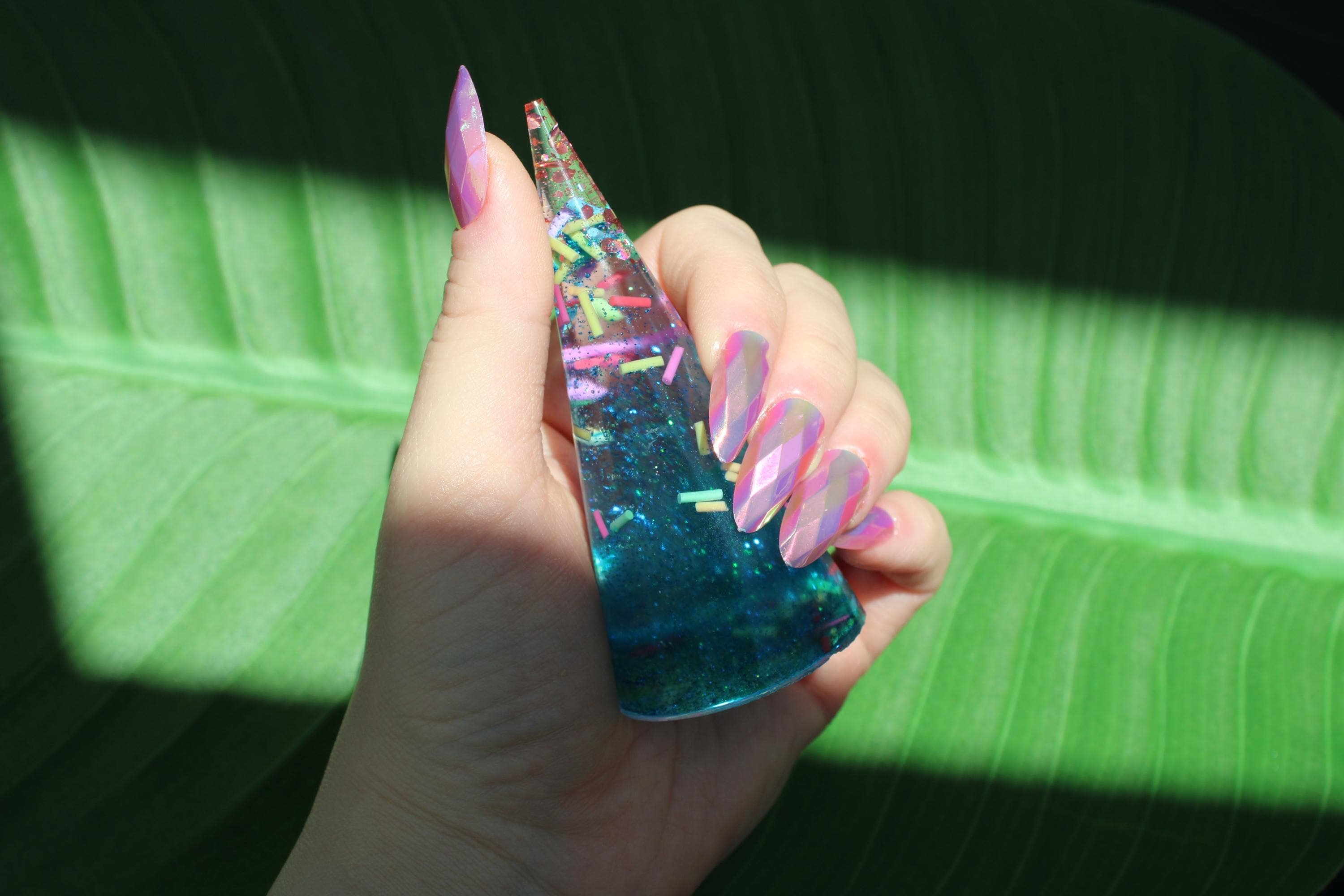 Photo shows a hand holding a ring display cone with sprinkles inside of it against a leafy background