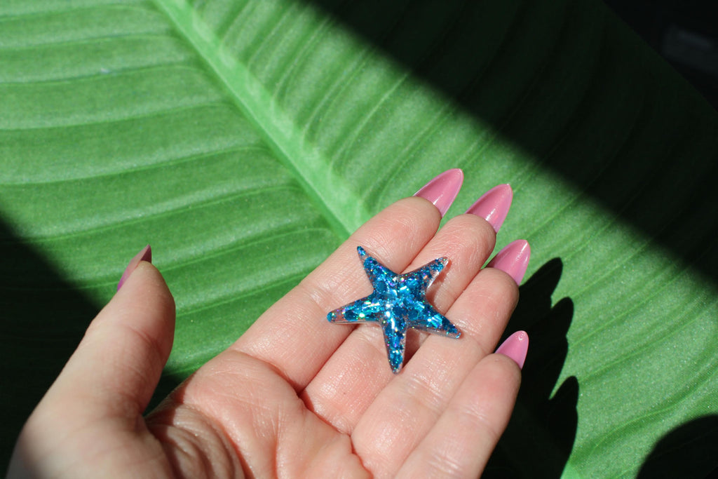 Hand holding a blue sequin resin starfish on a green leaf