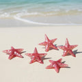 Pink glittery resin starfish on a sandy beach with ocean waves in the background
