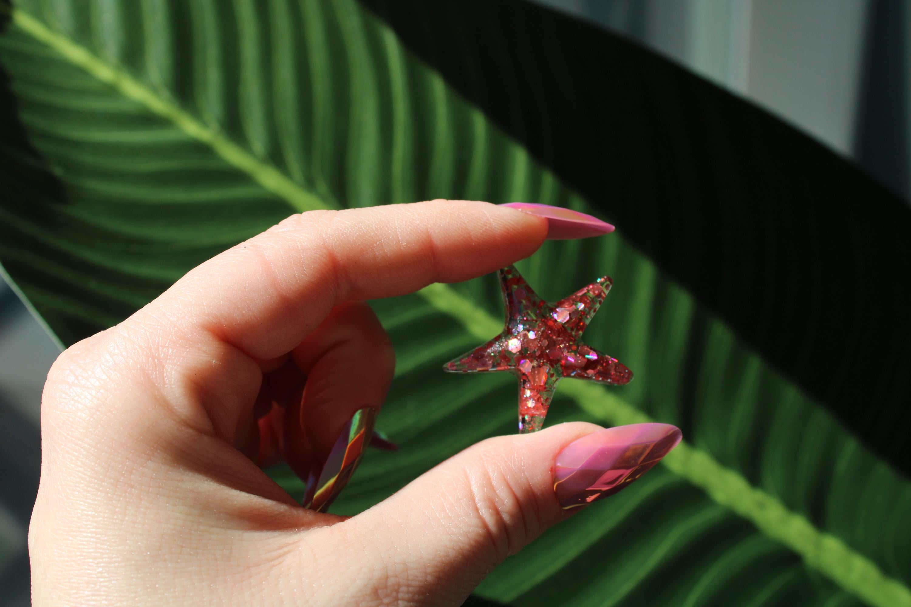 Hand holding a pink resin starfish against a green leafy background