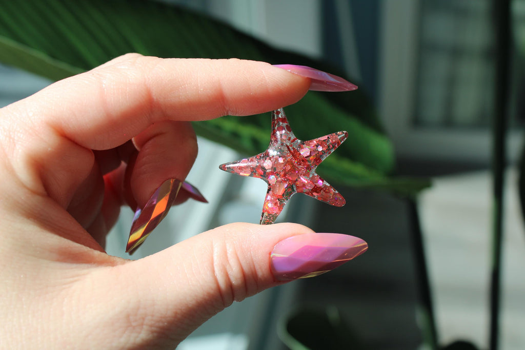 Hand holding a pink resin starfish object with blurred background