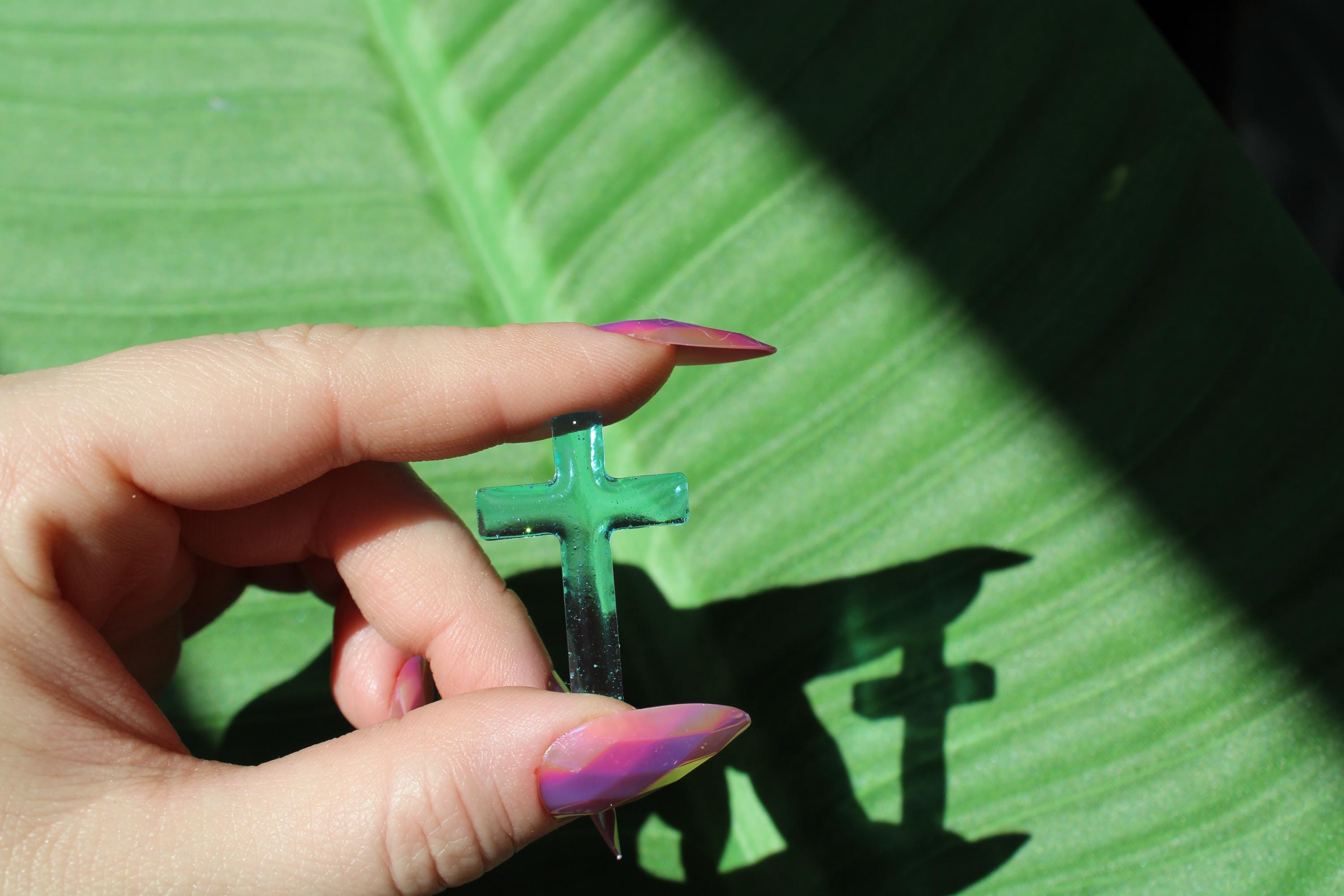 Hand holding a resin cross against a green leaf background