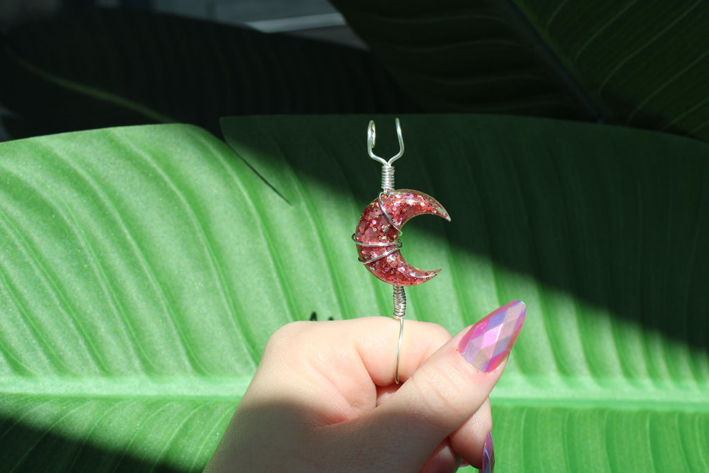 Hand holding a pink crescent moon smoke ring against a green leaf background