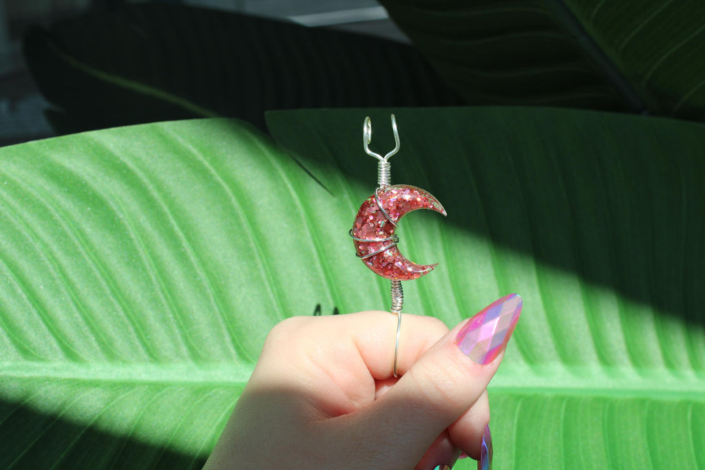 Hand holding a pink crescent moon smoke ring against a green leaf background