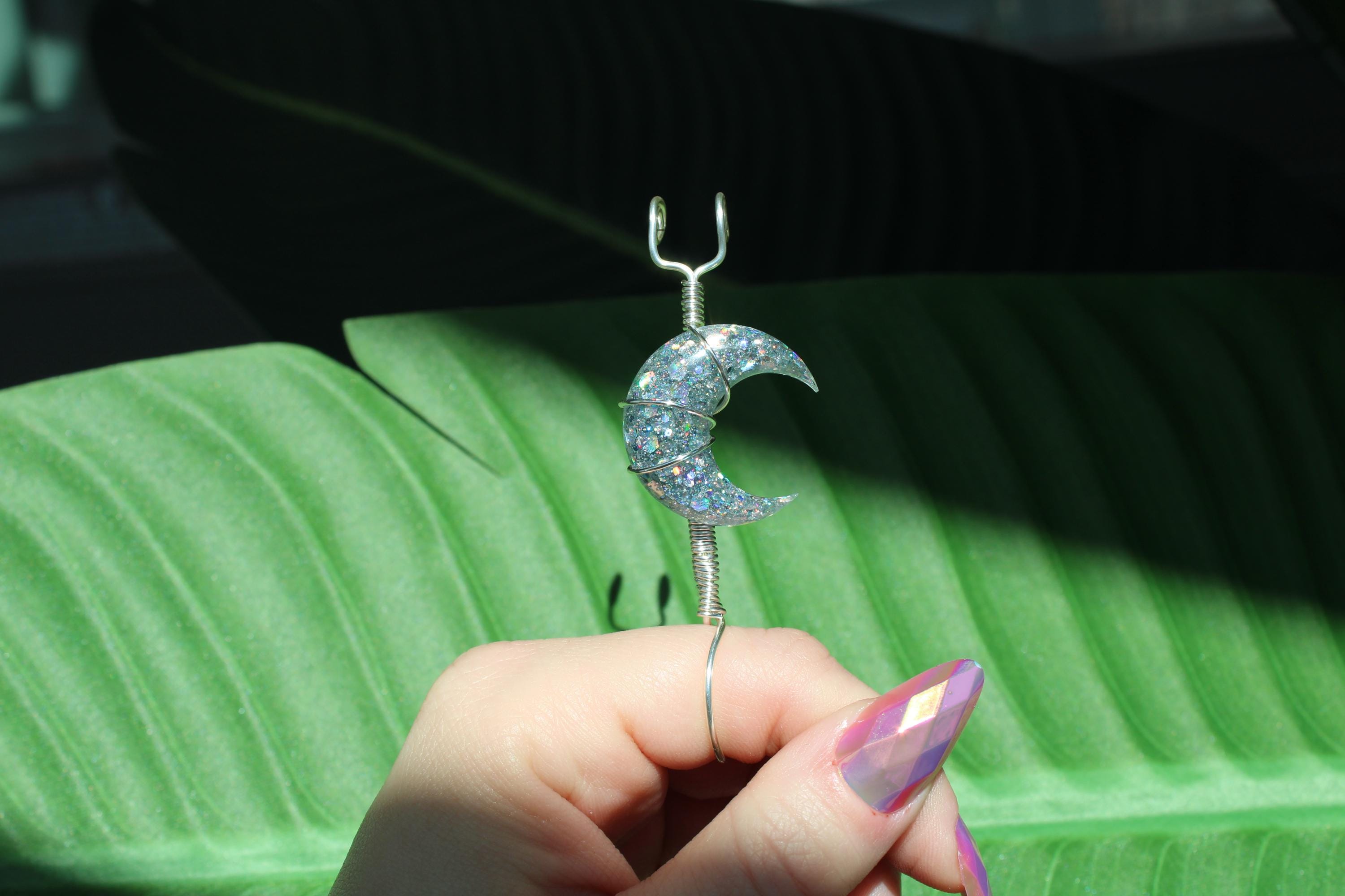 Hand holding a smoke ring with a crescent moon design against a green leaf background.