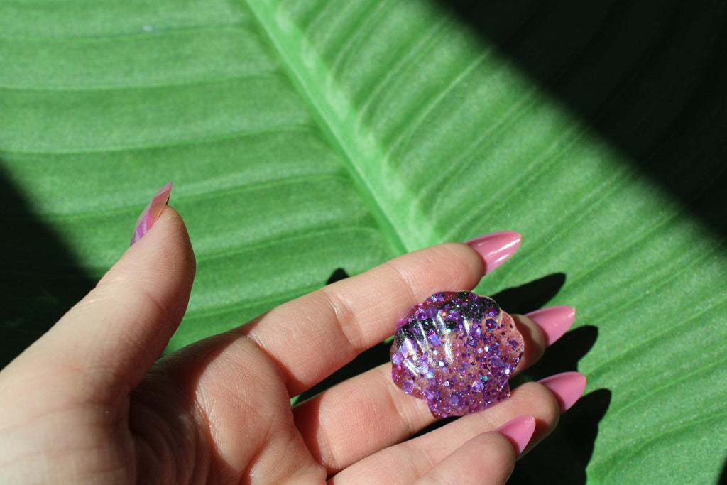 Hand holding a resin shell against a green leaf background