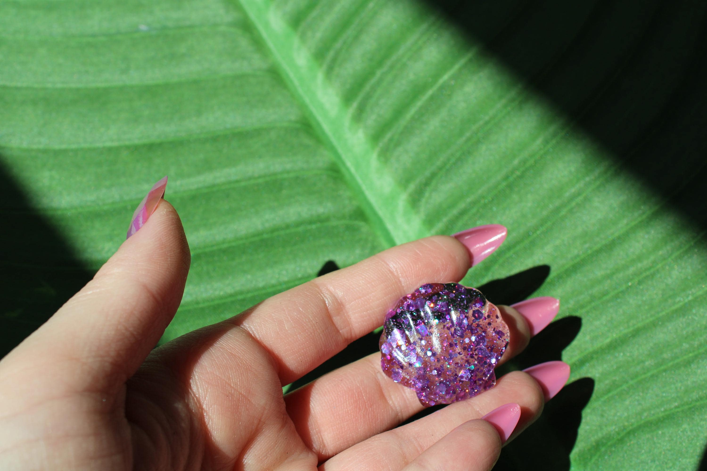 Hand holding a resin shell against a green leaf background