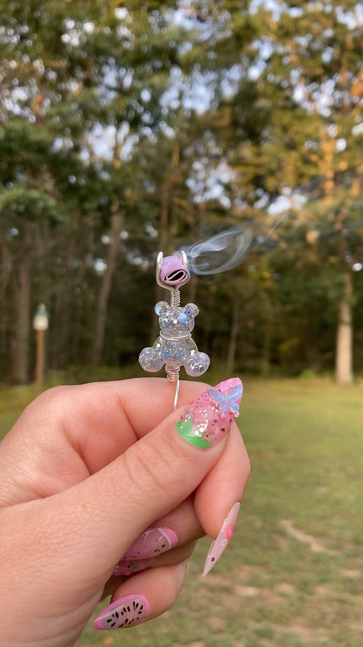 Video shows a sequin teddy bear smoke ring lit with a faux joint in a nature setting