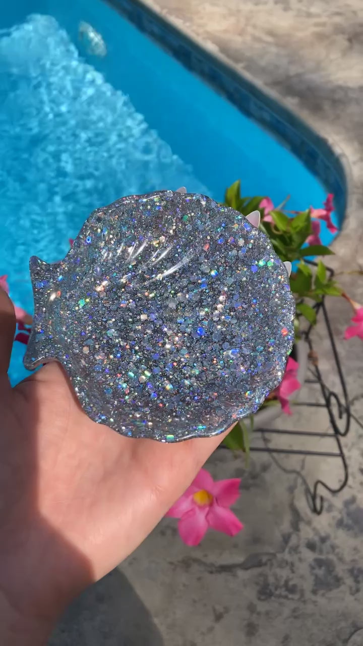 The video shows a sequin seashell soap dish on the edge of a pool held in a hand