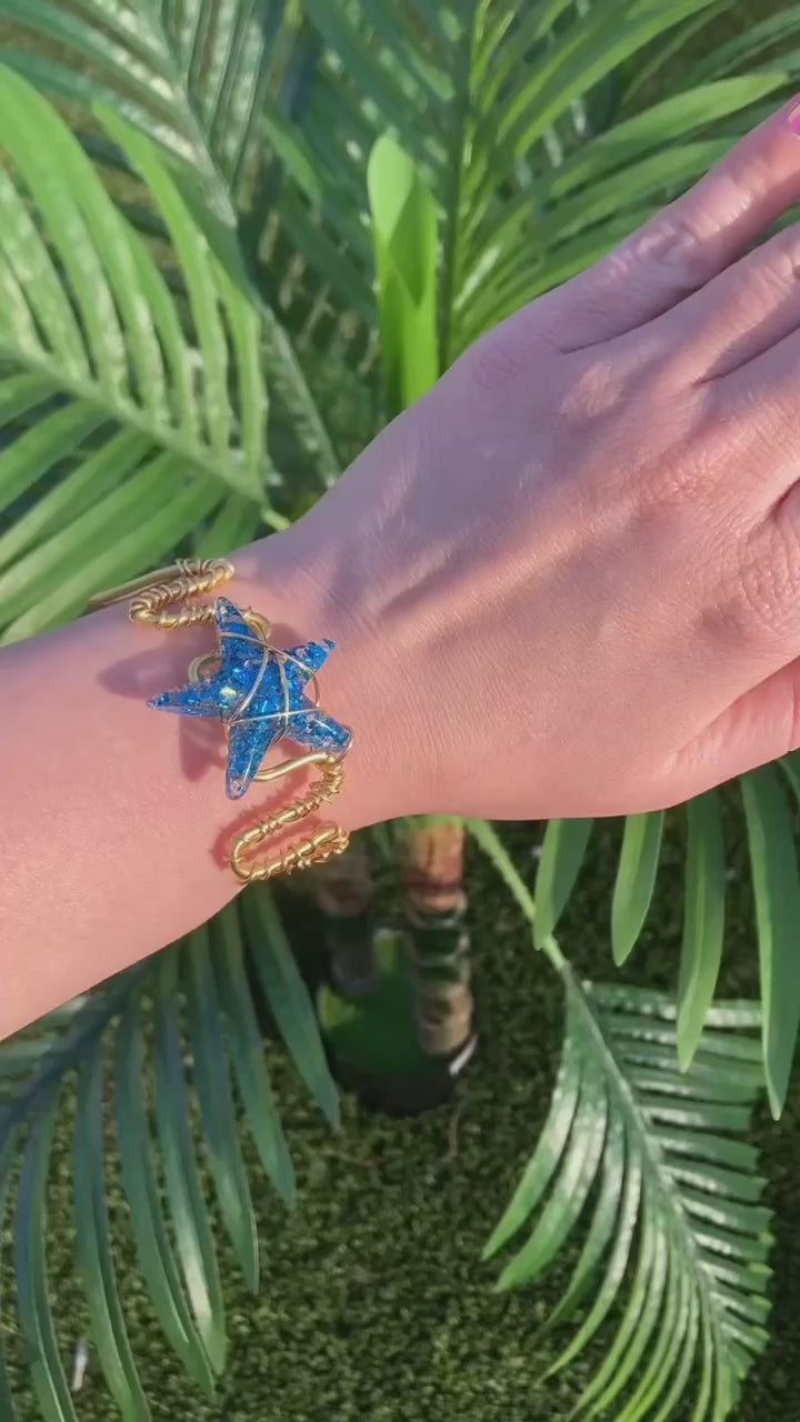 Video shows a blue sequin starfish wire wrapped copper bracelet on a hand in front of a fake plant