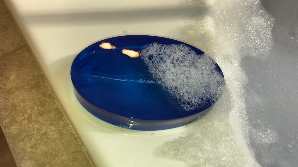 Video shows a blue modern oval soap dish with soap suds on it next to a jacuzzi tub