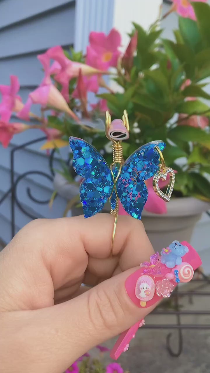Blue Butterfly Smoke Ring With Faux Joint Lit In Front Of Flowers.