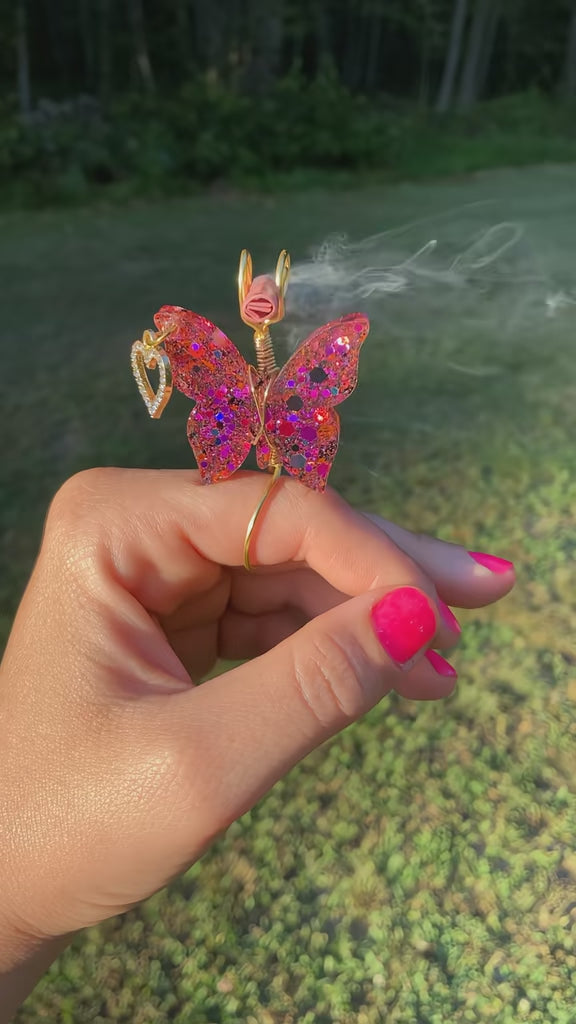 Video shows a butterfly smoke ring with black and pink sequins lit with a faux joint in a nature setting