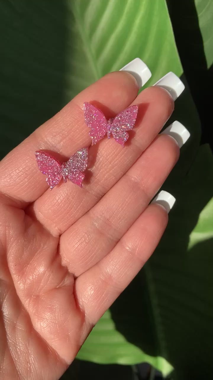 The video shows a hand holding pink butterfly stud sparkle earrings 