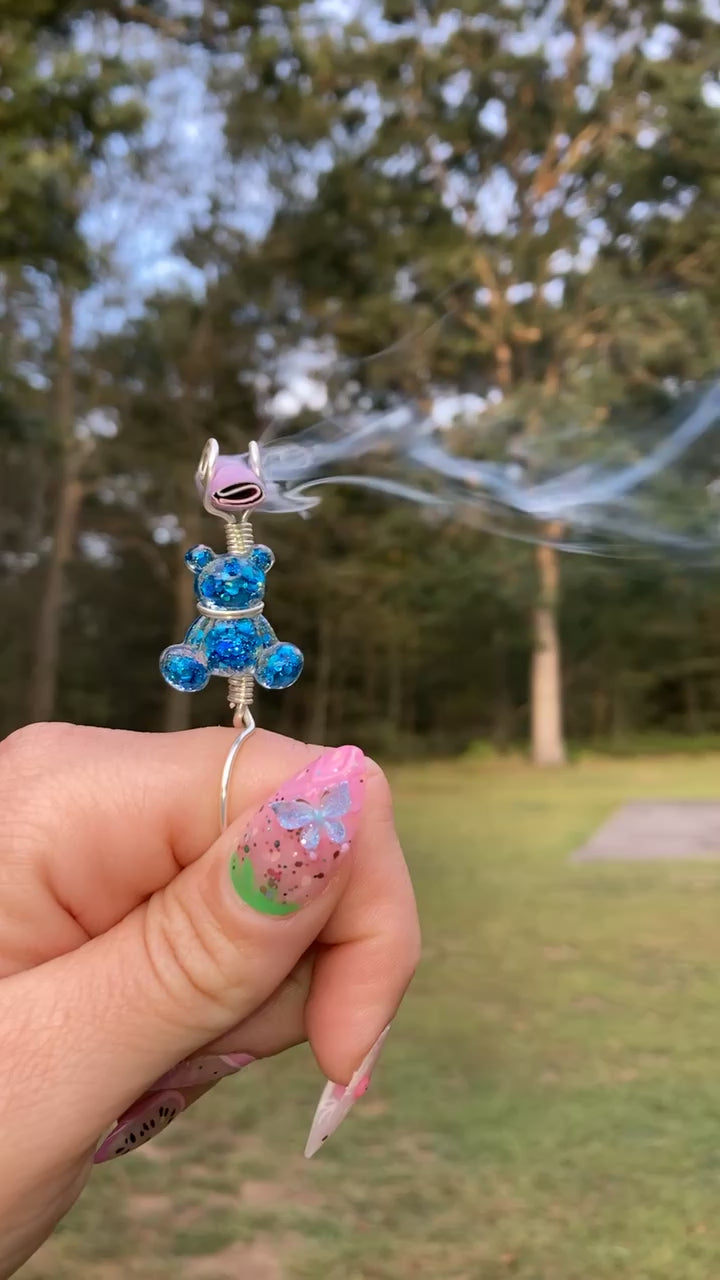 Video shows a blue sequin teddy bear smoke ring being lit with a faux joint in an outdoor setting