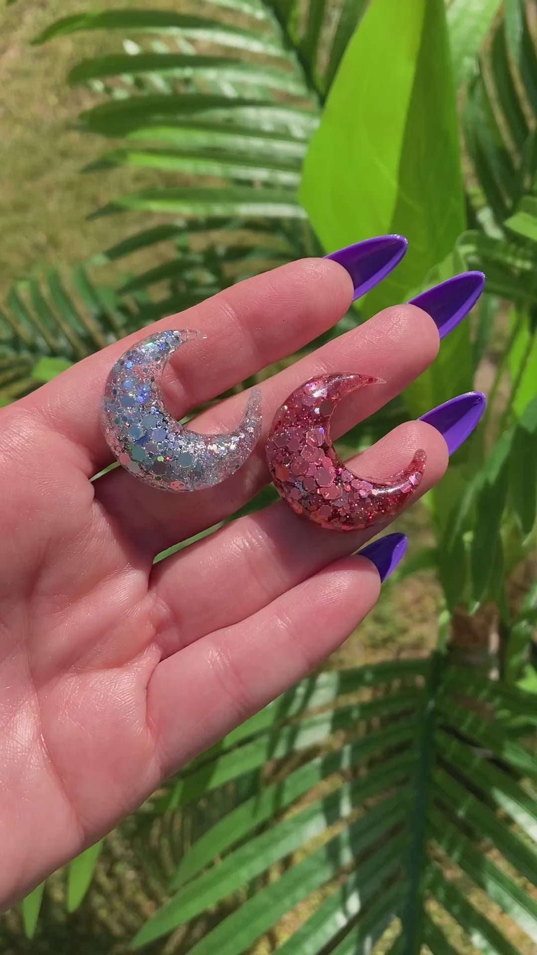 Video shows a hand holding two crescent moon car vent clips in front of a fake plant.