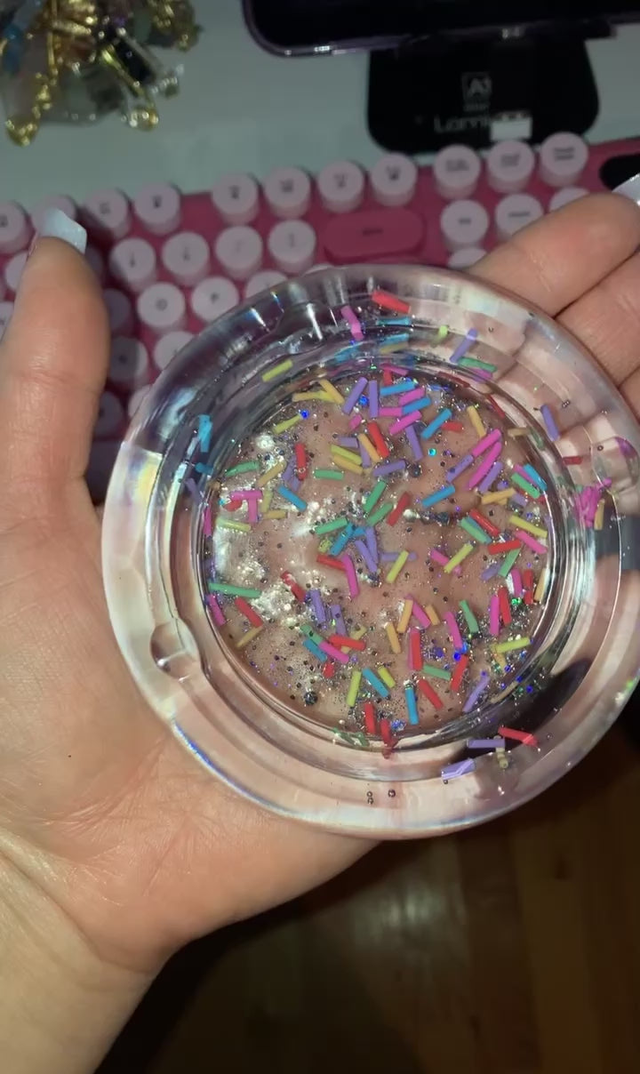 A hand holding a resin clear ashtray with sprinkles and glitter design.