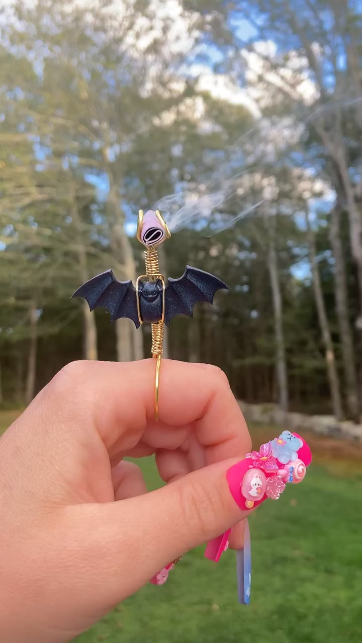 The video shows a black bat smoke ring lit with a faux joint in a nature setting.