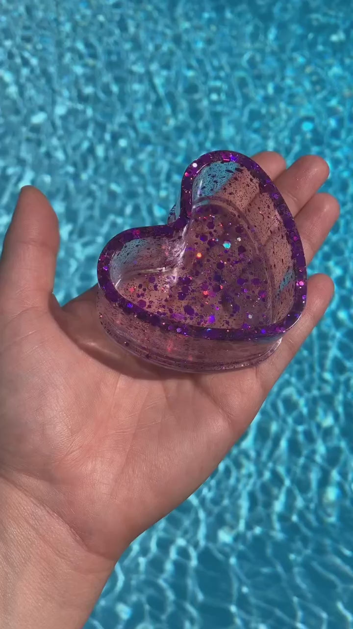 The video shows a small purple sequin heart ring dish in front of water.