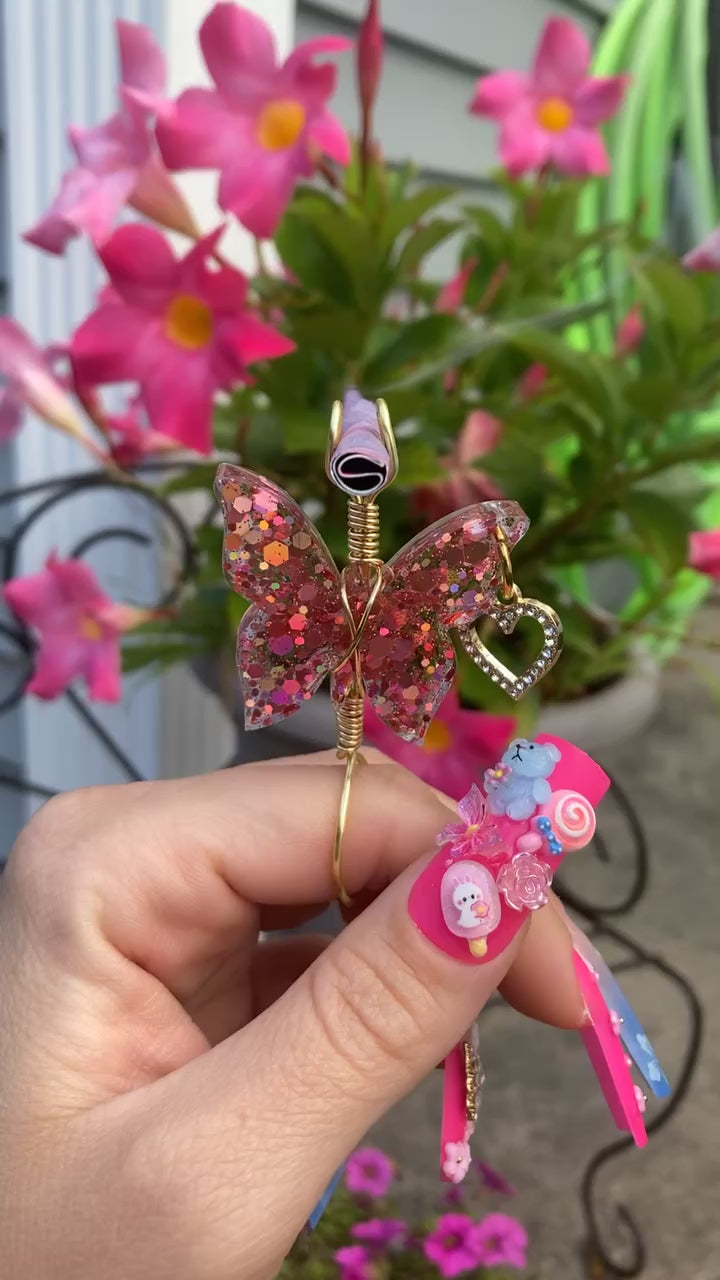 Pink sequin butterfly smoke ring with a lit faux joint in front of flowers.