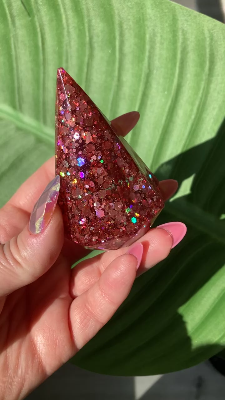 Video shows a pink sequin ring holder in a manicured hand in front of a leafy background 