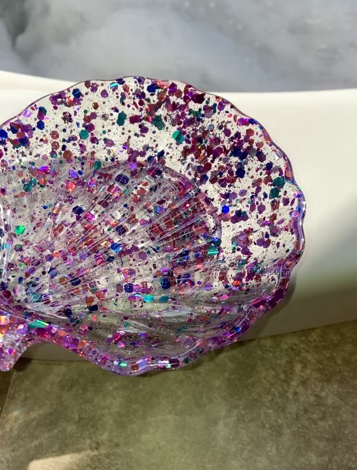 Video shows a mermaid colored seashell soap dish on the edge of a jacuzzi tub