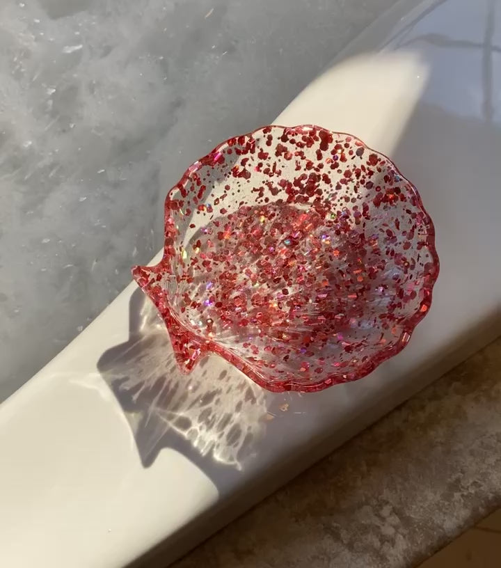 Video shows a light pink sequin shell soap dish on the edge of a tub