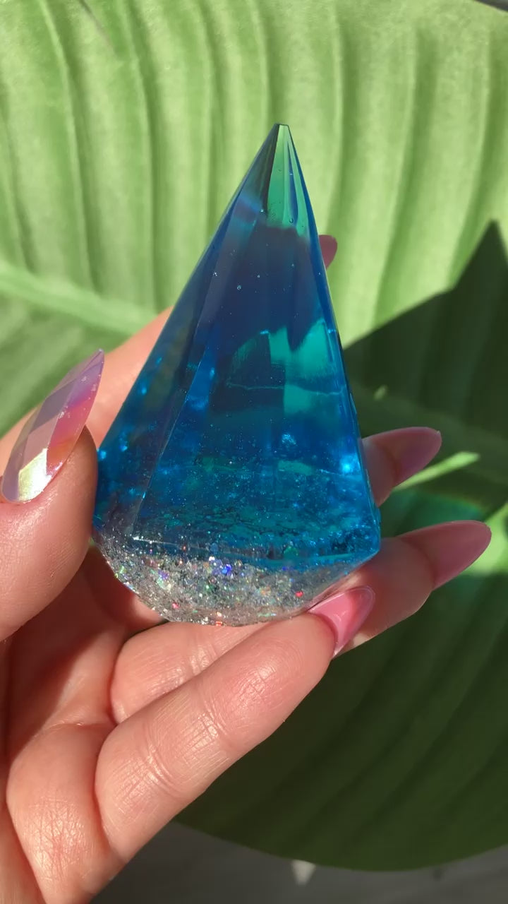 Video shows a blue ring display in a manicured hand in front of leafy background.